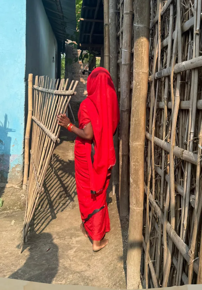 A woman in a red sari walking through a bamboo gate