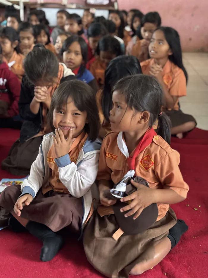 A smiling young girl in a school uniform sitting with her classmates