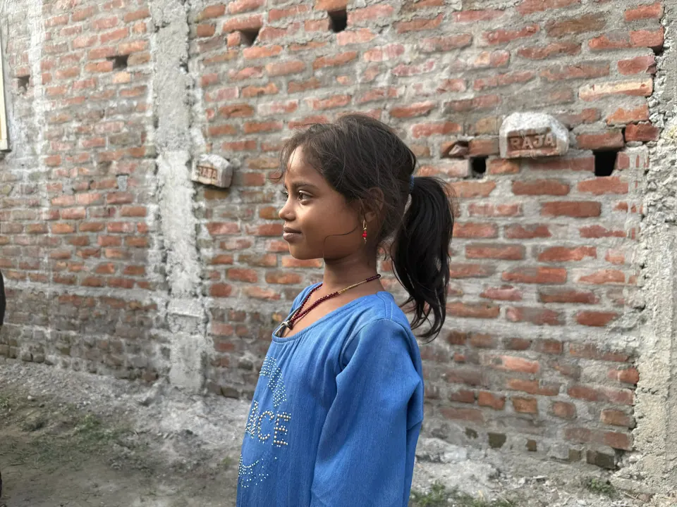 A young girl in a blue dress standing beside a brick wall