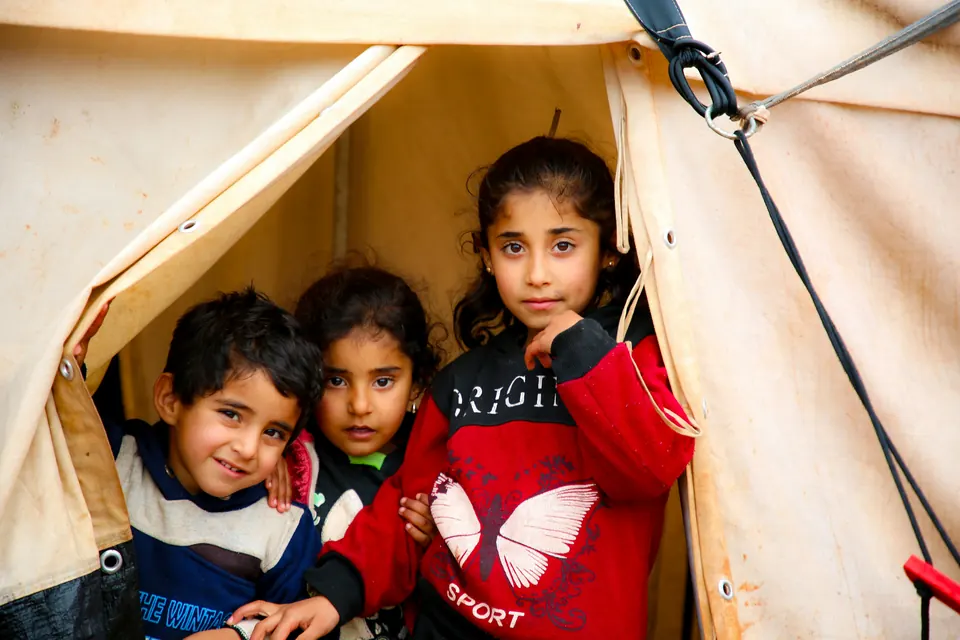 Three children smiling from the doorway of a tent