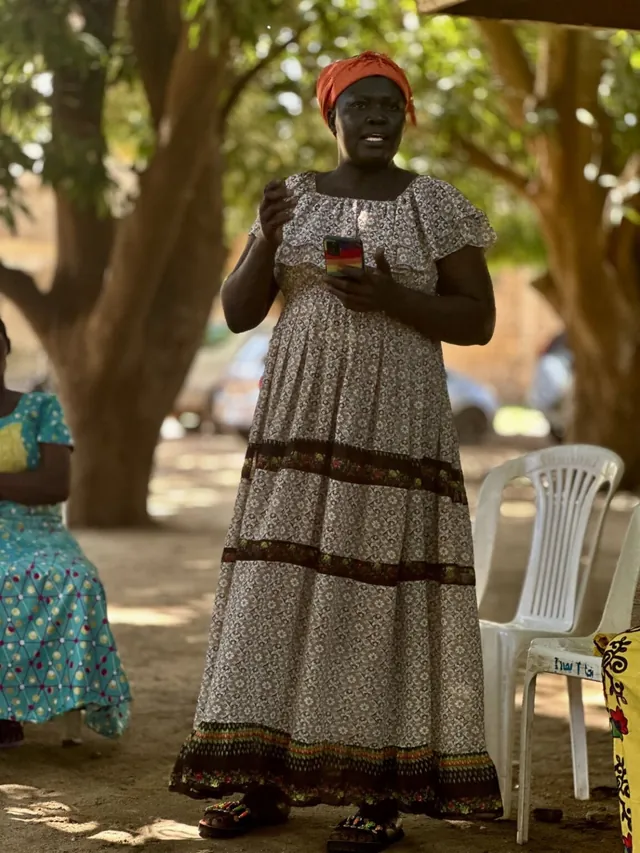A South Sudanese woman leader speaking under a tree