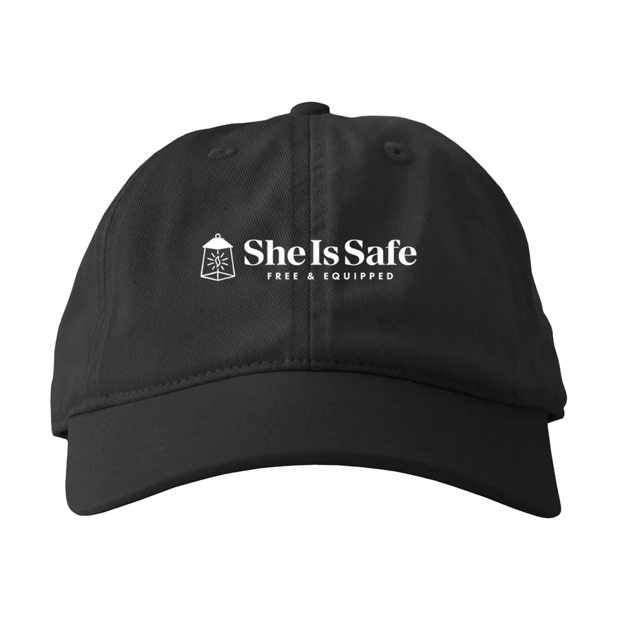 She Is Safe cap embroidered with the She Is Safe logo. Clicking the cap opens the Bonfire store in a new tab.